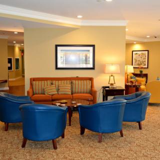 A cozy lobby seating area featuring blue chairs and a sofa arranged around a coffee table, with artwork adorning the walls.