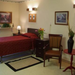 A cozy bedroom with elegant decor featuring a red bedspread, paintings on the walls, and a chair next to a lamp.