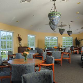 A well-lit dining area with multiple tables and chairs, featuring large windows and elegant lighting.
