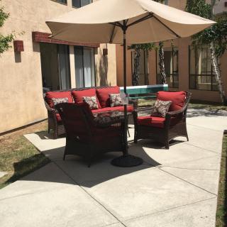 A sunny patio with red-cushioned outdoor furniture and an umbrella.