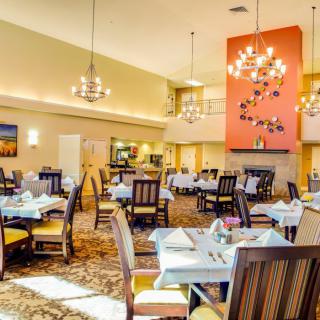A spacious dining area with elegant chandeliers, neatly arranged tables, and comfortable chairs.