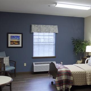 An inviting healthcare room featuring a bed, seating area, and natural light.