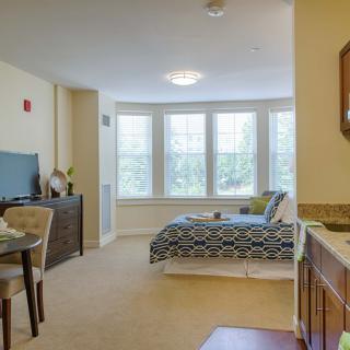 A cozy studio apartment featuring a bed, dining area, and large windows providing ample natural light.