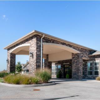 A well-maintained building with a stone facade and a covered entrance, surrounded by landscaping.