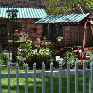 A cozy garden with a swing, colorful flowers, and a picket fence under striped awnings.