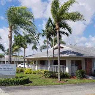 A charming residential building surrounded by palm trees under a partly cloudy sky.