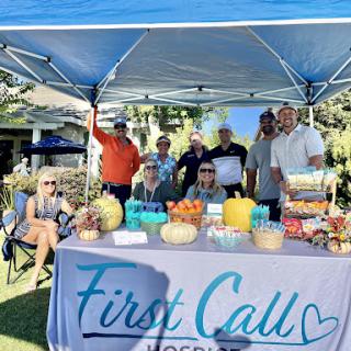 A vibrant community event showcasing the First Call booth with a variety of treats and a friendly group gathered under the sun.