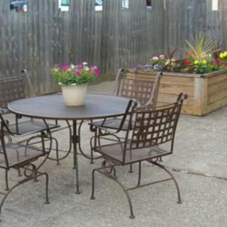 A cozy outdoor patio setup with metal table and chairs, surrounded by planters filled with vibrant flowers.