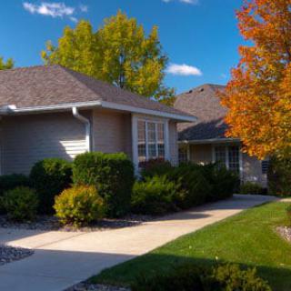 A suburban house surrounded by lush greenery and colorful autumn foliage under a bright blue sky.