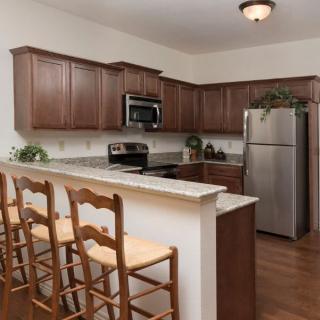 A modern kitchen with wooden cabinets, stainless steel appliances, and a breakfast bar with seating.
