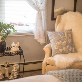 A cozy corner of a living room featuring an armchair with a pillow and blanket, next to a table with decorative items and a plant.