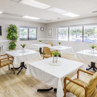 A bright and airy dining room with neatly arranged tables and chairs, decorated with plants.
