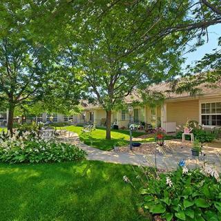 A serene garden setting with a lush lawn, mature trees, and a charming patio.