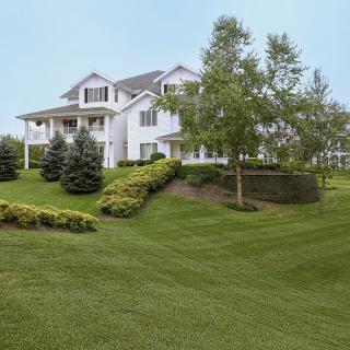 A large white suburban house with a well-manicured lawn and trees.
