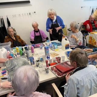 A group of seniors participating in an art class, with various painting supplies on the table.