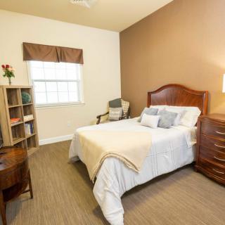 A cozy bedroom with a neatly made bed, wooden furniture, and a window letting in natural light.