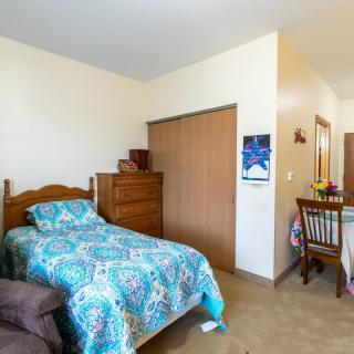 A cozy bedroom with a single bed and a dining area in view.