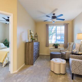A cozy interior space with a living area and an adjacent bedroom, featuring comfortable seating, a dresser, and soft lighting.