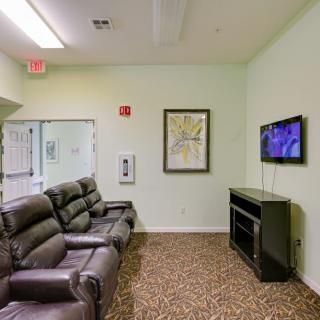 A cozy living room with recliner chairs facing a mounted television above a fireplace, featuring a carpeted floor and framed artwork on the wall.