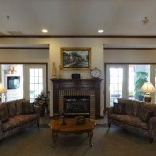 A cozy living room with a fireplace and two couches around a coffee table, adorned with lamps and a painting above the mantel.