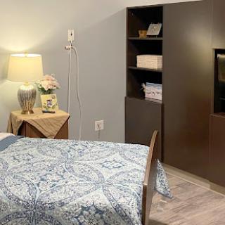 A cozy and modern bedroom featuring a neatly made bed with a blue patterned coverlet, a bedside lamp, and a stylish shelving unit.