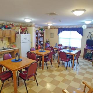 A cozy dining room with multiple tables and chairs, featuring a small kitchen area and warm decorations.
