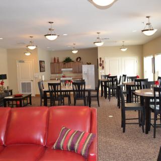 A modern lounge area featuring a red sofa, dining tables, and a kitchen in the background.