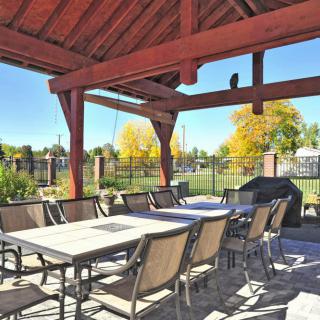 An outdoor patio with tables and chairs under a wooden gazebo in a sunny park setting.