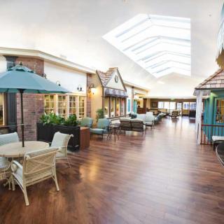 A spacious hallway with comfortable seating areas and a skylight, featuring tables and chairs along the sides.