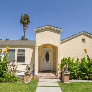 A charming single-story house with a well-maintained lawn and garden under a clear blue sky.