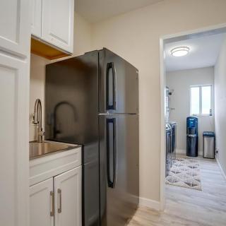 A modern kitchen with a black refrigerator, white cabinets, and an adjoining laundry room.