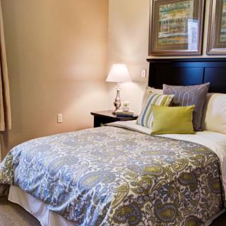 A cozy bedroom with a neatly made bed, decorative pillows, and a bedside lamp.