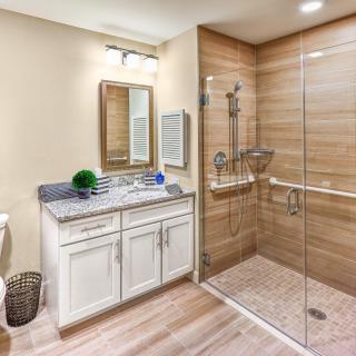 A modern bathroom with wooden accents featuring a spacious glass-enclosed shower, a large mirror above the sink, and a stylish vanity.
