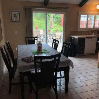 A dining room with a large table and chairs, adjacent to a kitchen and sliding glass doors leading outside.