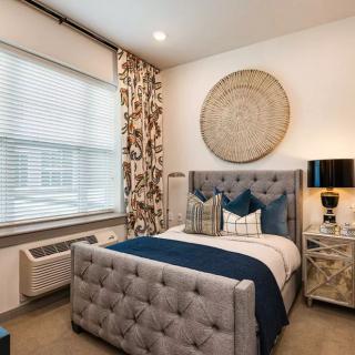 A modern bedroom featuring a tufted bed with blue and white pillows, complemented by stylish wall art and a sleek lamp.