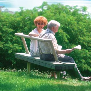 An elderly couple sitting on a bench in a park, enjoying a leisurely time with greenery around them.