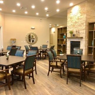 A cozy dining area with multiple tables and chairs, featuring a fireplace and warm lighting.