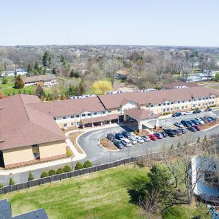 Aerial view of a large building with a parking lot in a suburban setting surrounded by greenery.