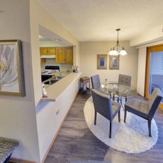 A modern dining area with an open layout leading to the kitchen, featuring a round glass table and upholstered chairs.