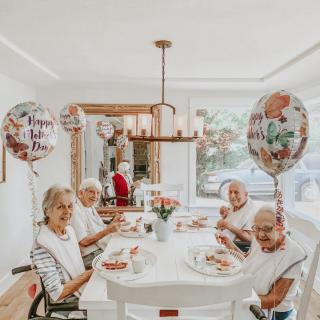 A group of elderly women enjoying a meal together, surrounded by festive balloons in a cozy dining room.