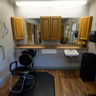 A compact barber shop interior featuring a styling chair, mirror, wooden cabinets, and a sink.