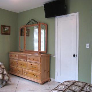 A bedroom with a wooden dresser and mirror, a wall-mounted TV, and green walls.