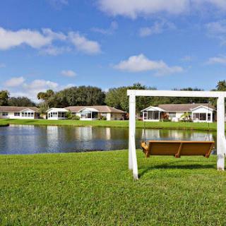A serene park with a swing overlooking a tranquil lake, surrounded by residential homes.