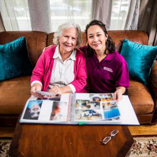 A joyful moment shared between a caregiver and an elderly woman as they look through a photo album together.