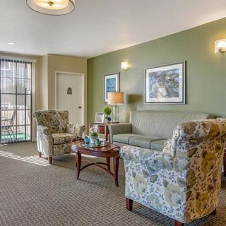 A cozy living room with floral-patterned chairs, a sofa, and a central table complemented by artwork and a lamp.