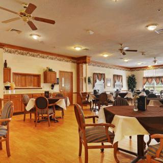 A warmly lit dining area with neatly arranged tables and chairs, featuring ceiling fans and wood flooring.
