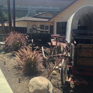 A historical covered wagon displayed outdoors near a ranch-style building with desert plants.