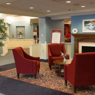 A cozy lobby seating area with red chairs arranged around a small table, featuring a fireplace and decorative elements.