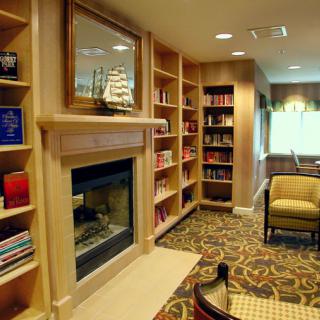 A cozy library with bookshelves, a fireplace, and comfortable seating.