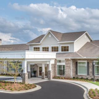 A modern residential building with a landscaped entrance and clear skies.